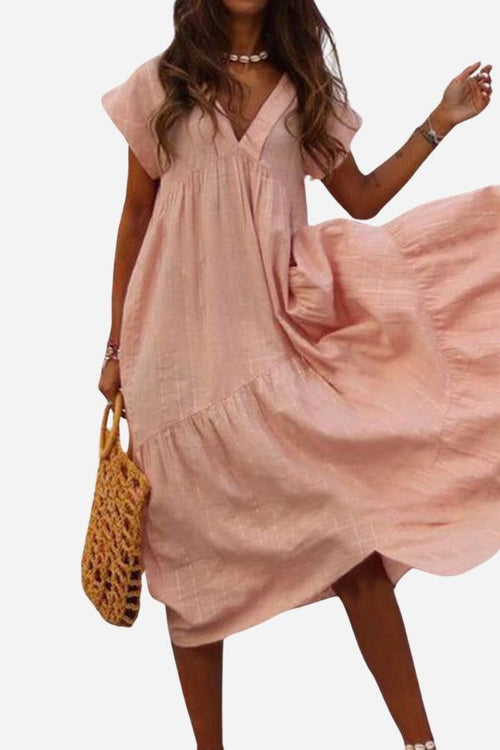 Woman wearing pink V neck tiered cotton midi dress with short sleeves and frill hem holding woven bag