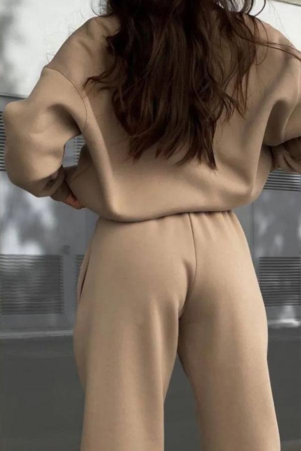Woman wearing beige cotton-blended two-piece tracksuit from back, featuring high collar and long sleeves, model outdoors.
