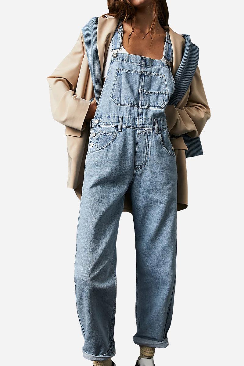 Woman wearing denim-look tapered-leg adjustable bib overalls with a beige jacket and blue sweater draped over shoulders