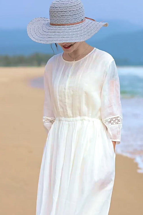 woman wearing white 100% linen coastal shift dress with lace sleeves and wide brim hat on beach