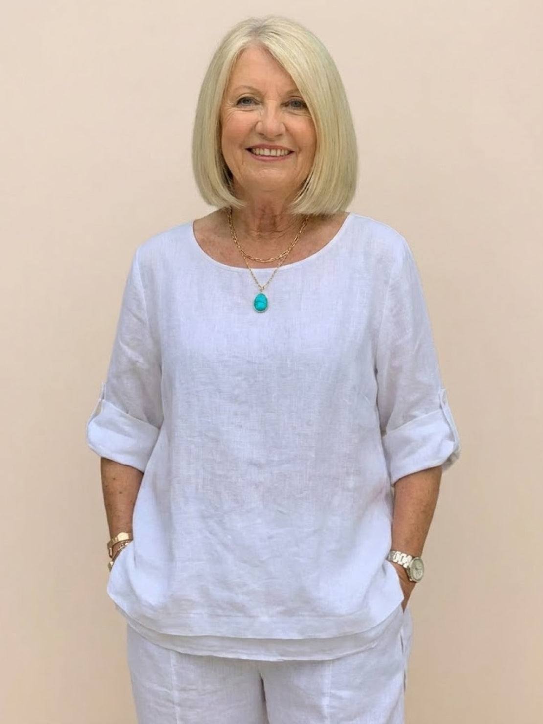 Older woman wearing a white asymmetrical two-piece trouser set with rolled-up sleeves and a relaxed fit.