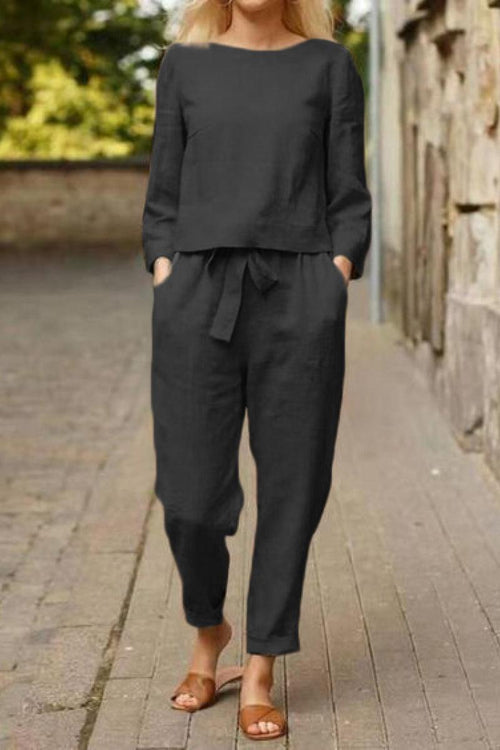 Woman wearing a black Cotton-Linen Monochrome Capsule relaxed longline top and wide-leg pants set with a tie waist, standing outdoors on a paved street.