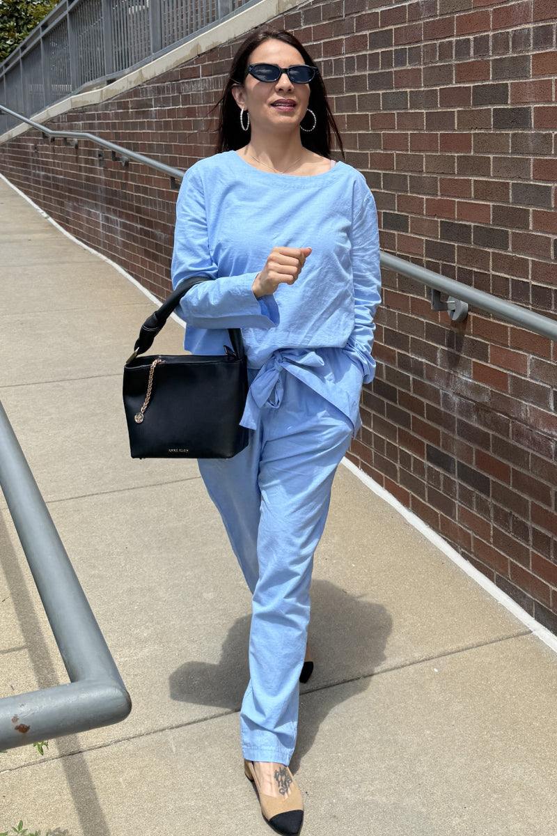 woman wearing light blue cotton-linen monochrome capsule outfit walking outdoors with black handbag and sunglasses