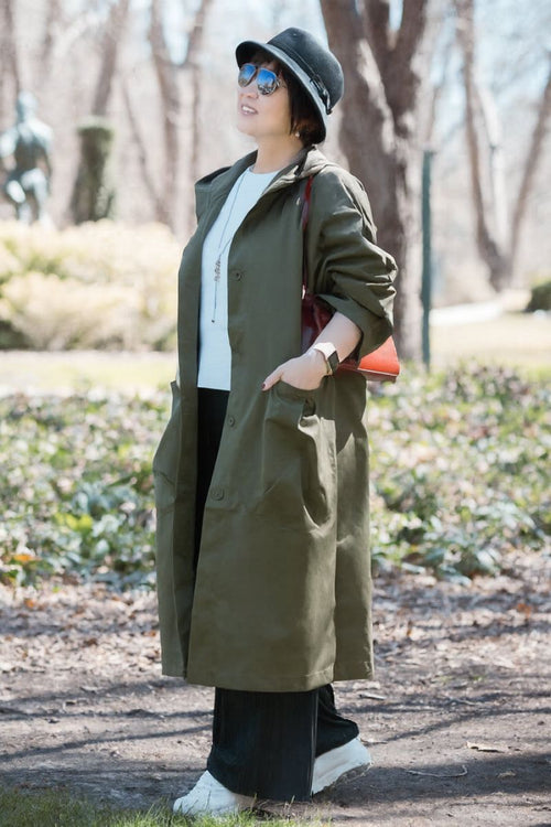 Woman wearing oversized olive green water resistant windbreaker jacket with hood and large pockets outdoors