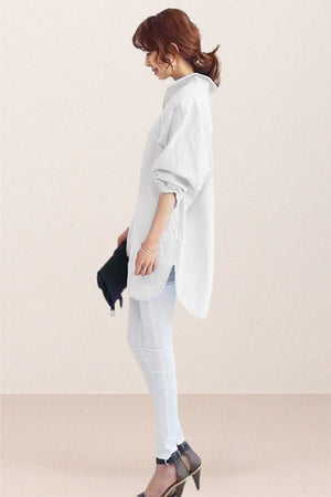 Woman wearing white oversized linen shirt with loose sleeves and flowing hemline, styled with white pants and heels.