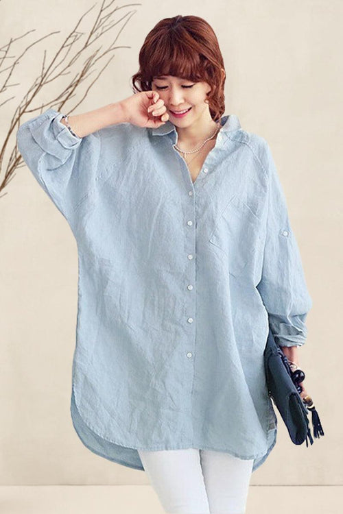 Woman wearing oversized light blue linen shirt with rolled sleeves and white pants