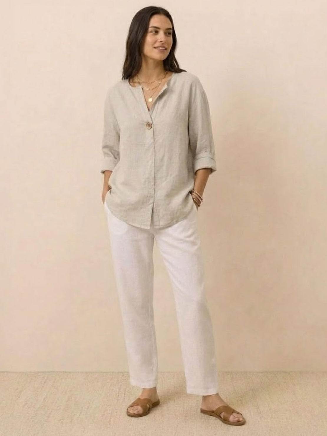 woman wearing pure linen age-defying button detail shirt with white pants and sandals standing against beige background