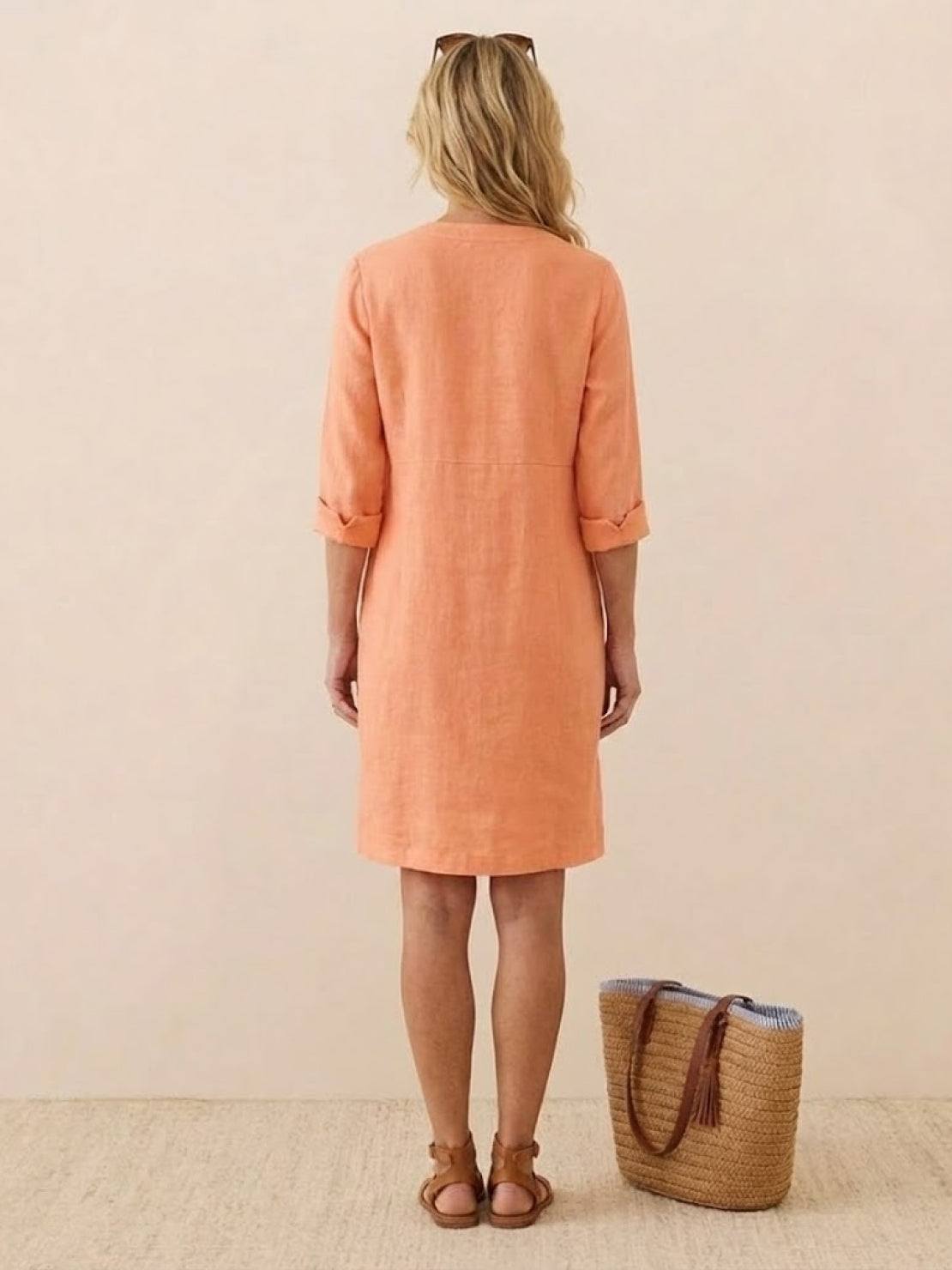woman wearing peach cotton dress with rolled 3/4 sleeves standing next to woven handbag