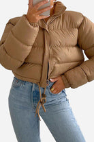 Brown cropped puffer jacket with high collar and drawstring hem, worn with light blue jeans