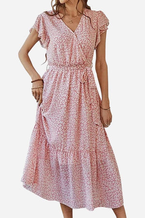 Woman wearing an Elegant Blossoms Boho Maxi Dress in soft pink floral wrap design with V-neck and belted ruffle hem