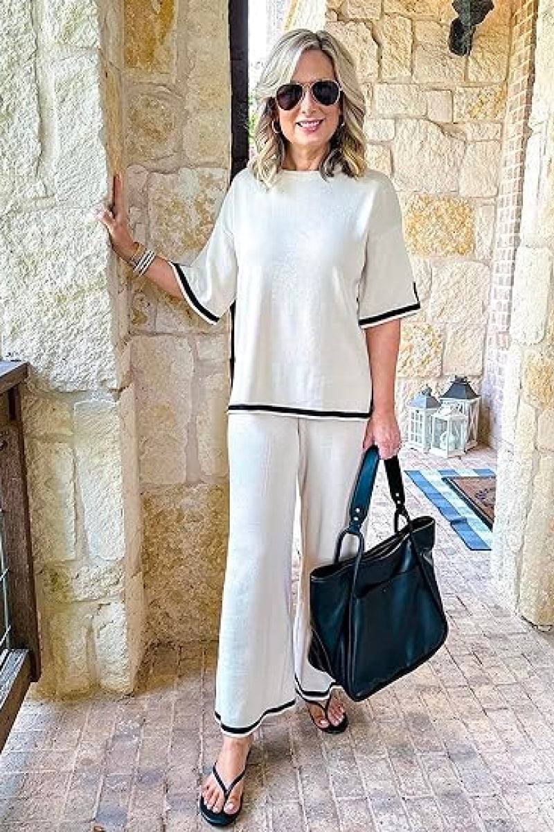 Woman wearing short sleeved relaxed fit lounge two-piece set with wide-leg pants and black trim, holding black handbag.