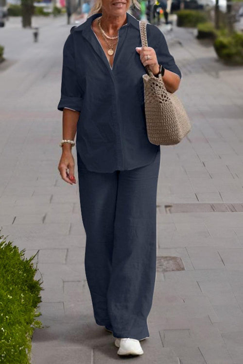 Woman wearing a navy relaxed shirt and trousers two-piece set walking on a city sidewalk carrying a beige woven bag