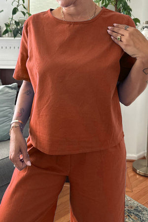 Woman wearing rust-colored loose fit co-ord set with short sleeves and wide-leg pants indoors