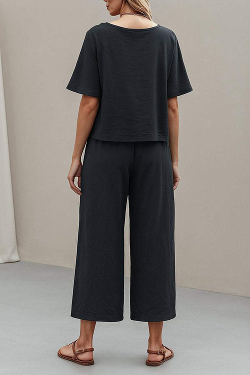 Back view of a woman wearing a black loose fit co-ord set with wide-leg pants and short-sleeve top.