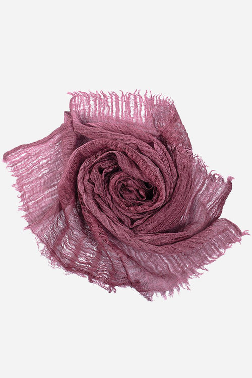 Lightweight linen scarf in dusty rose with frayed edges, folded in a rose shape