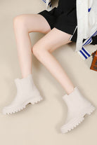 Light beige non-slip rain boots with chunky soles worn with black shorts and a white cardigan
