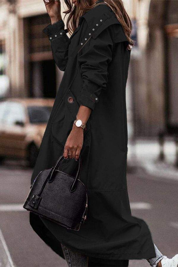 Woman wearing a black sleek minimalist hooded coat with oversized fit carrying a black handbag on city street