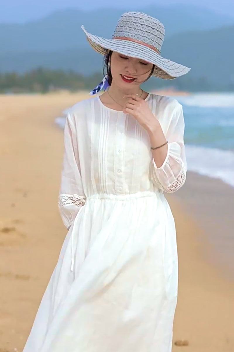 Woman wearing a white 100% linen coastal shift dress with long sleeves and lace details on a beach.