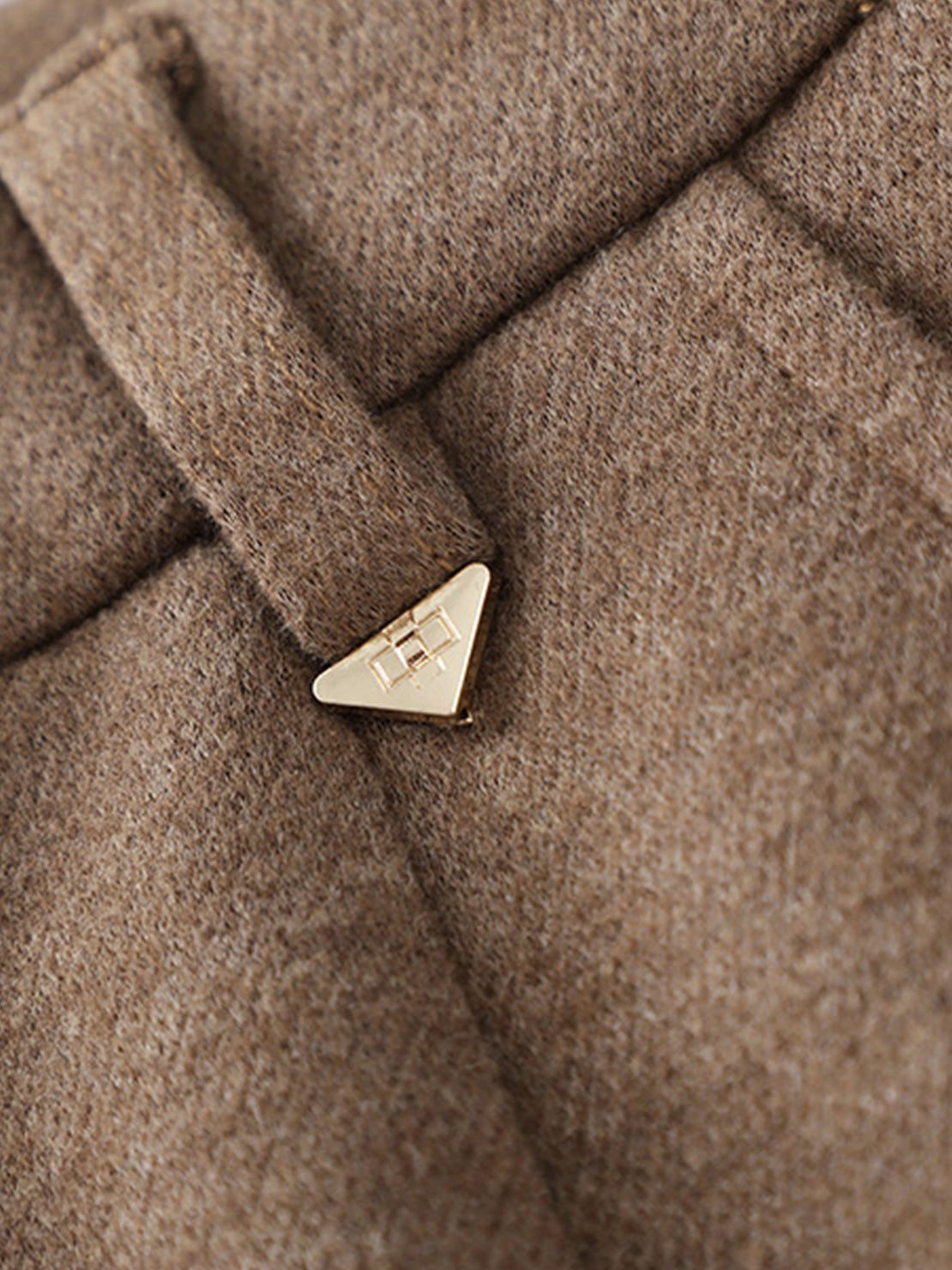 Close-up of brown thermal wool blend trousers fabric with gold triangular logo detail