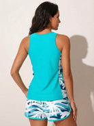 Woman wearing a racerback two-piece tankini set with scoop neckline and mid-thigh swim shorts in tropical print