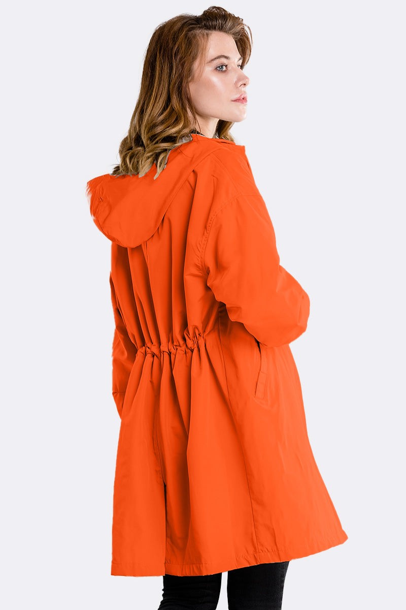 Woman wearing orange water resistant oversized hooded windbreaker rain jacket back view