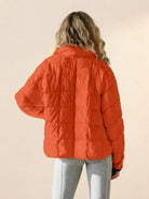 Back view of a woman wearing an orange lightweight puffer travel jacket with quilted design and long sleeves.