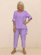Woman wearing lavender asymmetrical two-piece trouser set with rolled sleeves and tapered pants