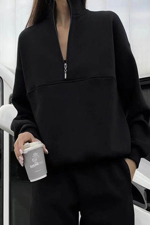woman wearing black Classic Airplane Set two-piece tracksuit with half-zip pullover and tapered joggers holding a coffee cup