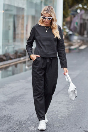 Woman wearing black cotton-linen monochrome relaxed longline top and wide-leg pants set with white sneakers and sunglasses walking outdoors