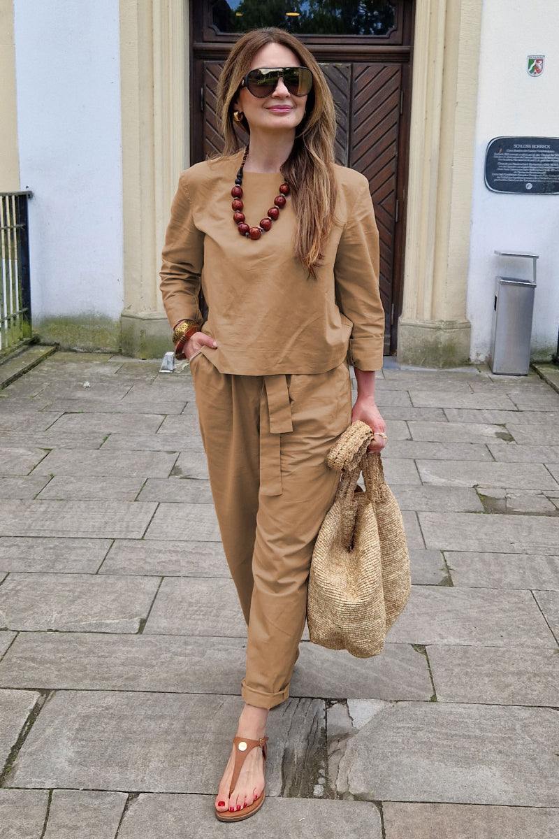 Woman wearing cotton-linen monochrome longline top and wide-leg pants set with brown necklace and woven bag outdoors