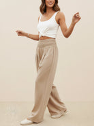 Women wearing beige high-waist linen cotton palazzo pants with a white sleeveless top and white shoes against a plain backdrop