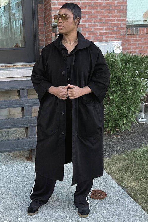 Oversized black water resistant windbreaker jacket with snap buttons and hood worn outdoors