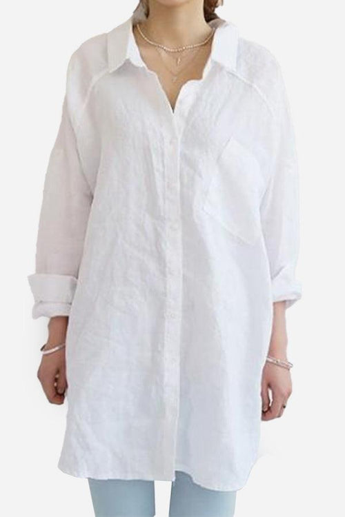 White oversized linen shirt with long sleeves, collared neck, and front pocket, styled casually with rolled cuffs.
