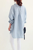 Back view of woman wearing light blue oversized linen shirt with rolled sleeves and white pants
