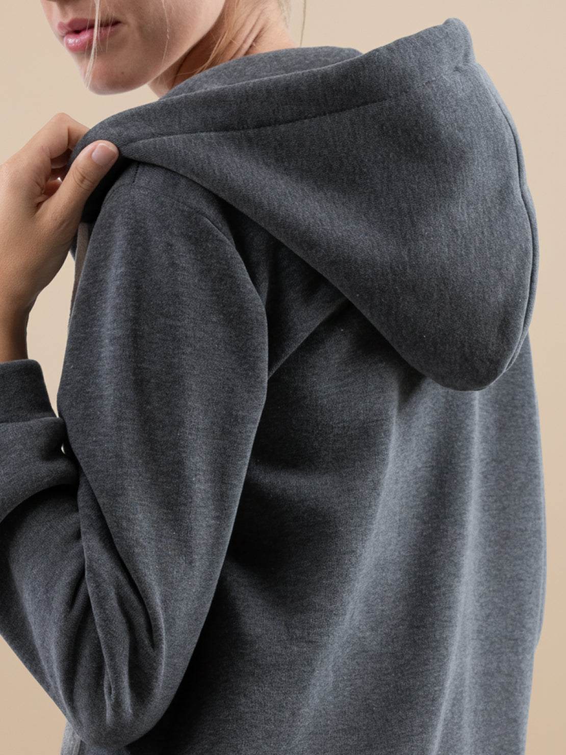 woman wearing oversized long zip sweatshirt hoodie in dark gray with hood up, casual cozy fleece-lined zip-up pullover