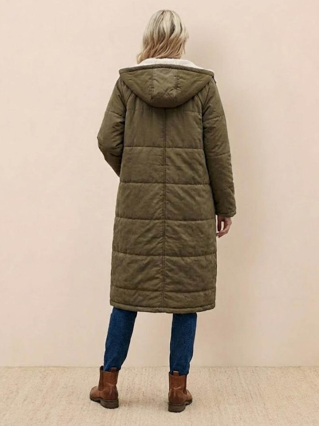Woman wearing olive green sherpa-lined hooded teddy coat with quilted puffer design and large pockets, paired with jeans and brown boots, back view