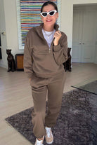Woman wearing a brown cotton blend tracksuit with a half-zip pullover and matching pants indoors
