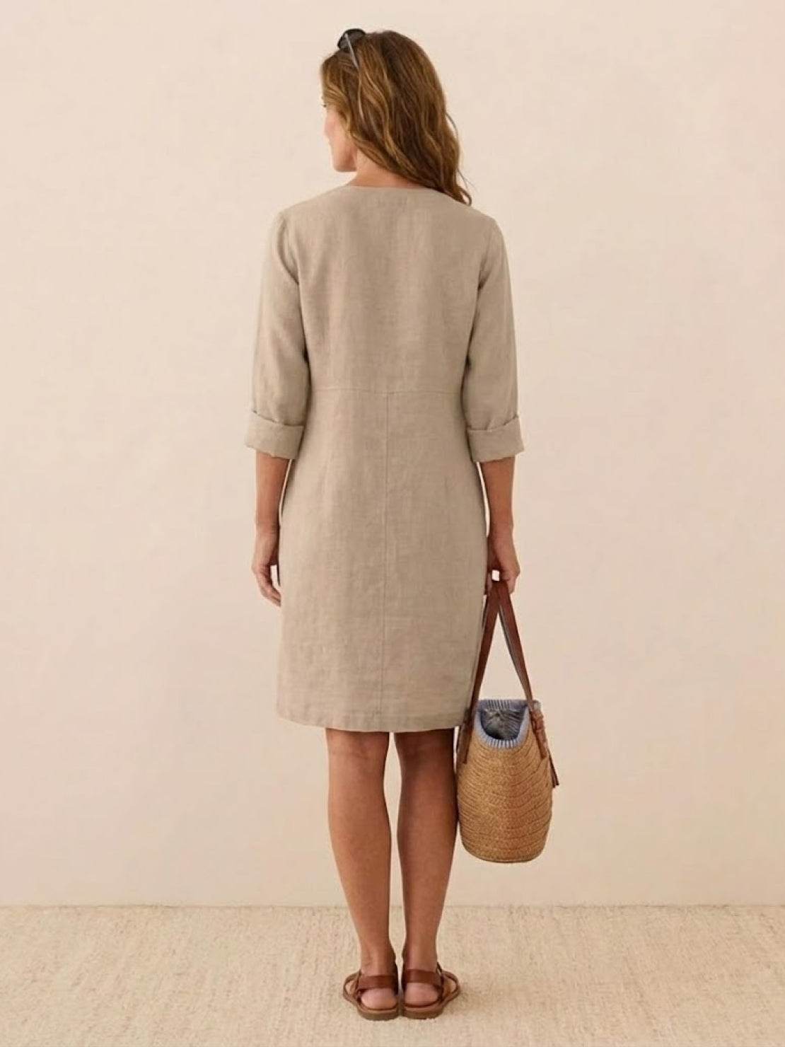 Back view of woman wearing timeless class cotton dress in khaki with 3/4 rolled sleeves carrying a woven handbag