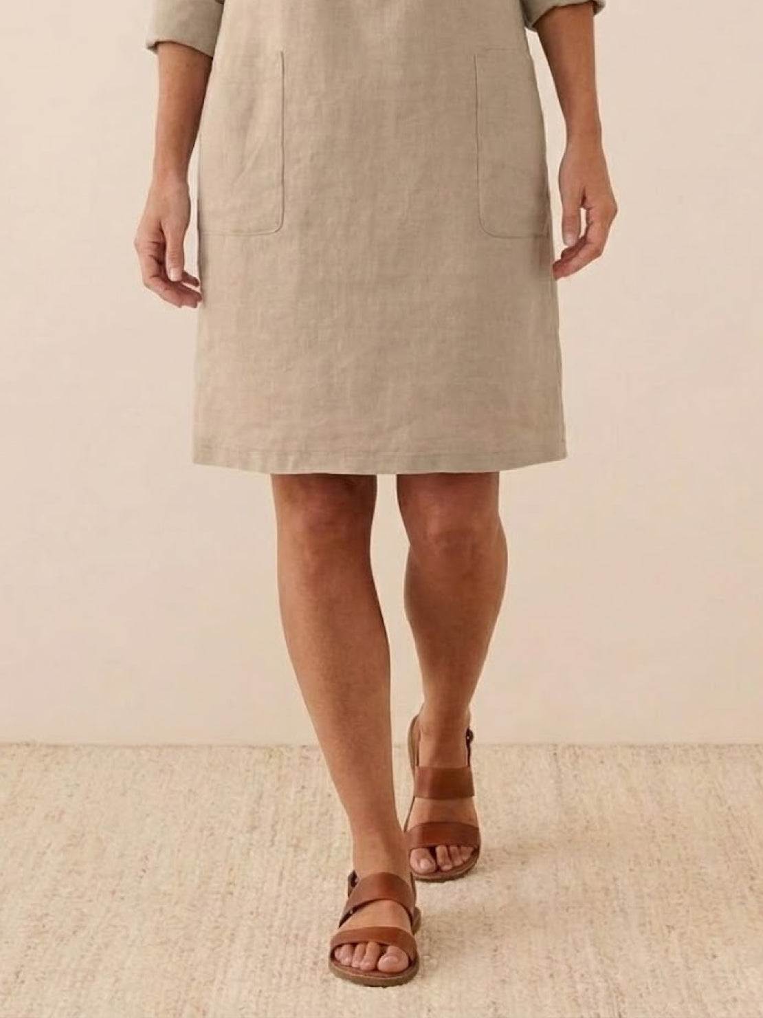 Beige cotton dress with pockets, knee-length and 3/4 sleeves rolled below elbow, styled with brown sandals, perfect for summer comfort and understated elegance.