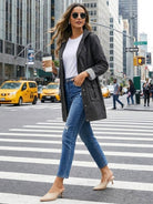 Woman wearing a black water resistant hooded windbreaker with striped detail walking in city street with coffee cup