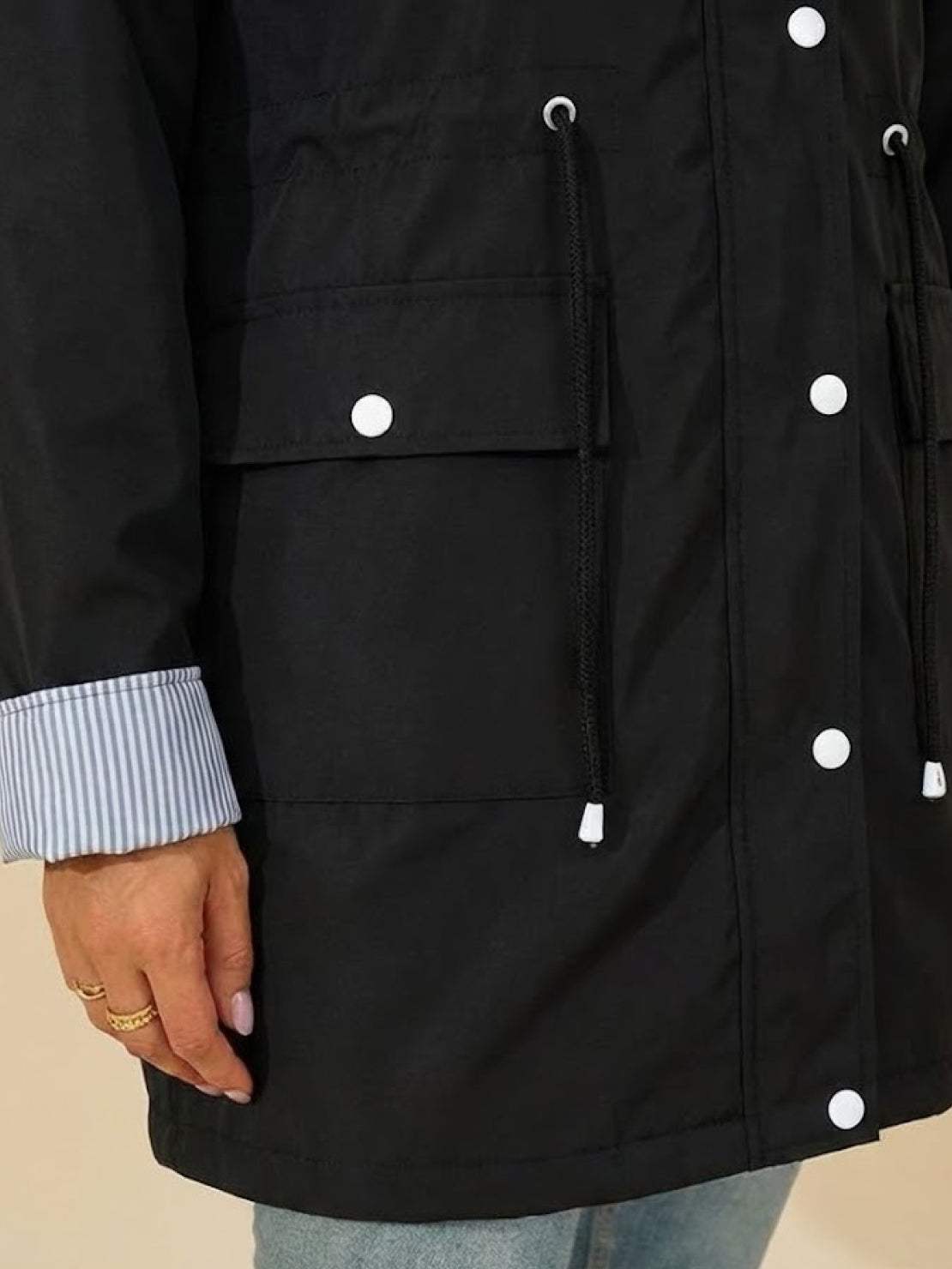 Close-up of black water resistant windbreaker jacket with button snaps and drawstrings on pocket and hood, featuring striped sleeve cuff.