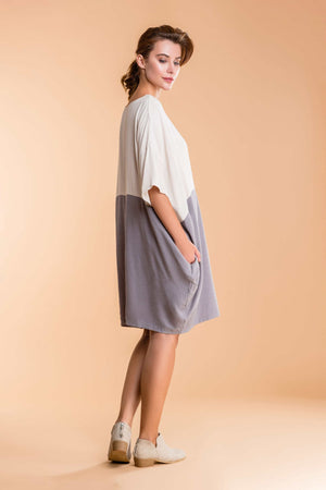 Side view of a woman wearing a loose fit oversized T-shirt dress in cream and gray color block with hidden pockets